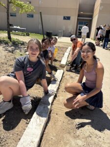 5 students and one adult volunteer squat to pose with pavers that were installed into the walkway during a grant workday at Gorzycki Middle School.