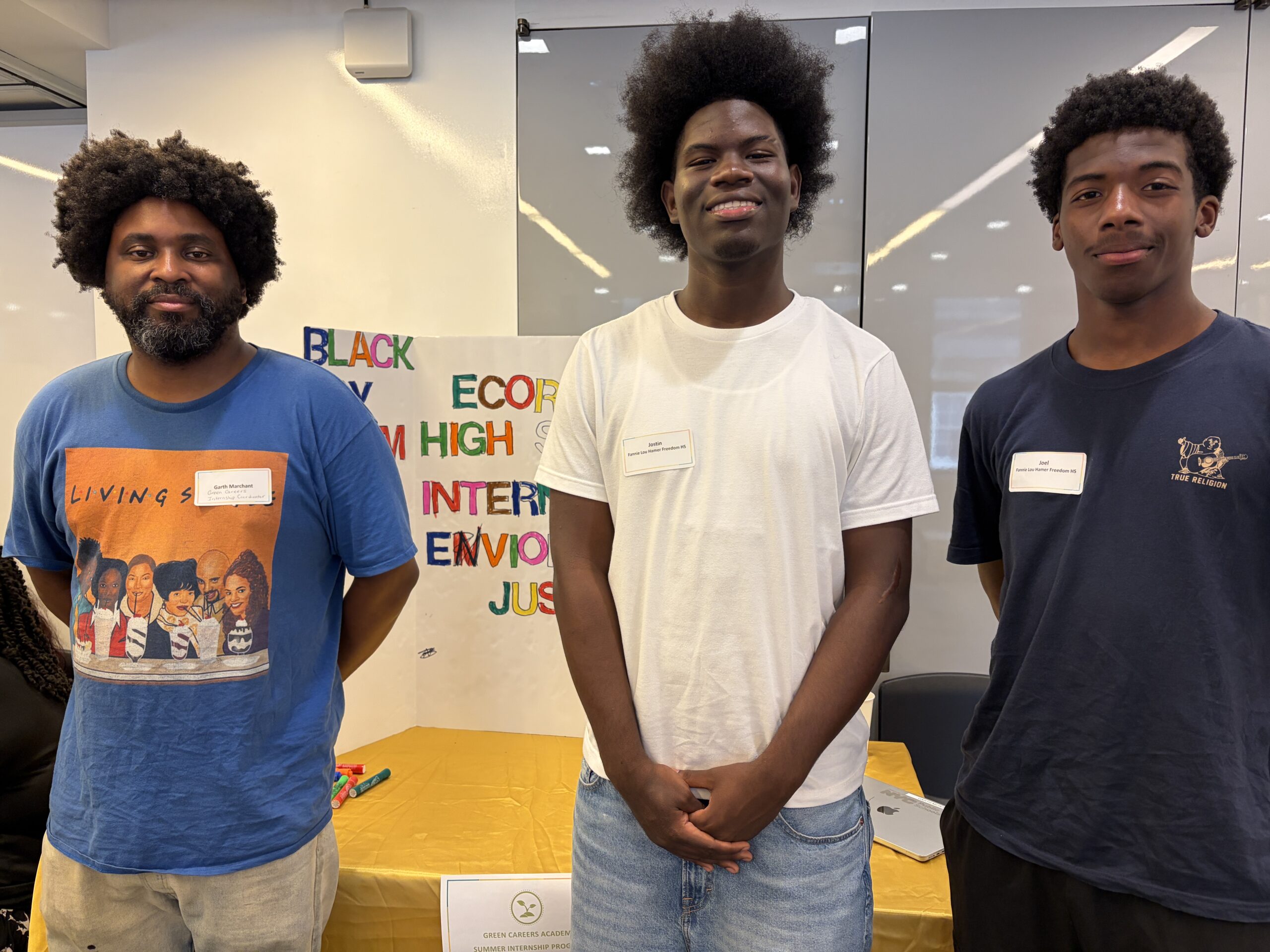 Teacher Garth Marchant and interns, Jostin and Rashaun, stand in front og a tri-fold board they created to share about their internships with The Black Feminist Project.